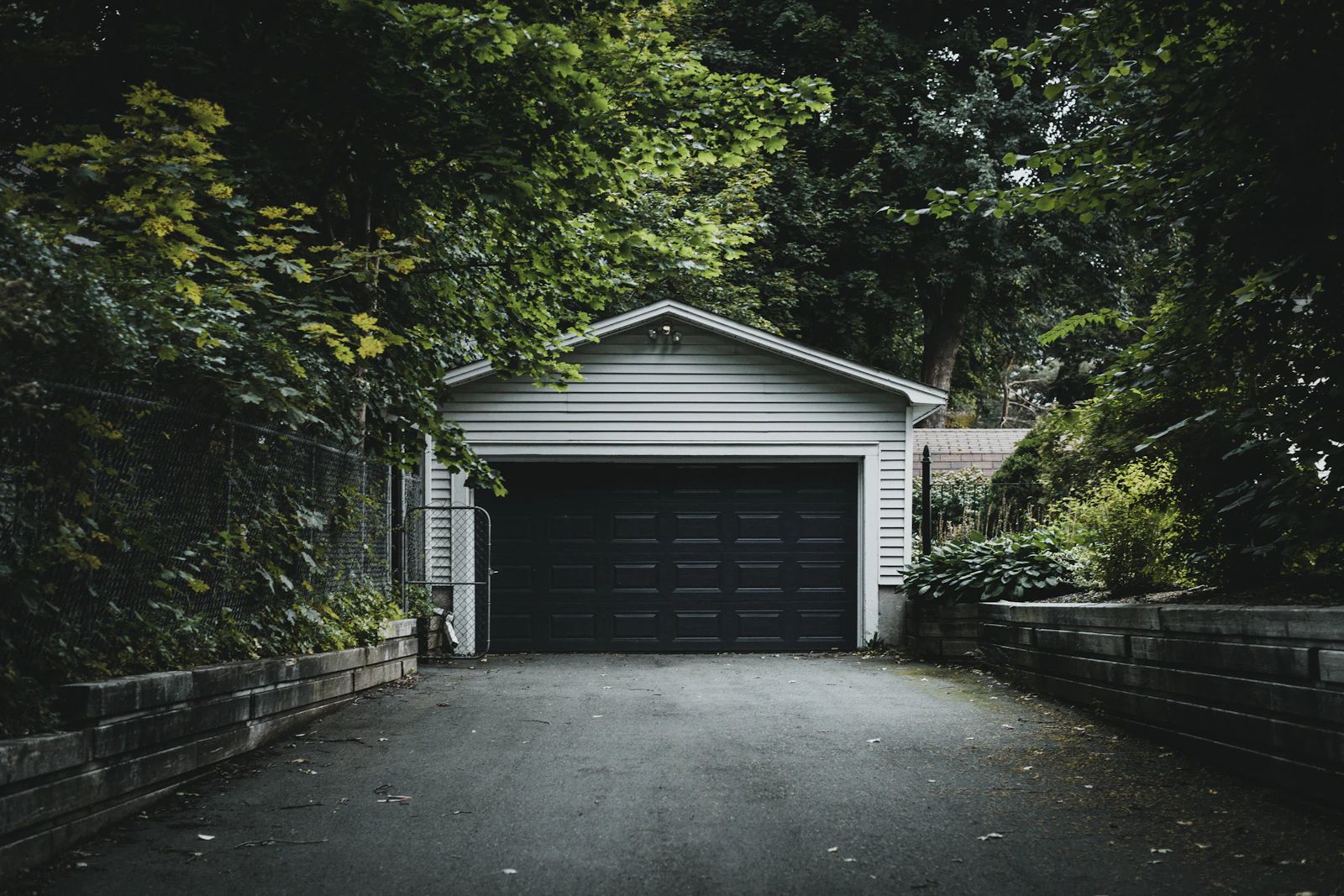 A detached garage with a dark door at the end of a driveway